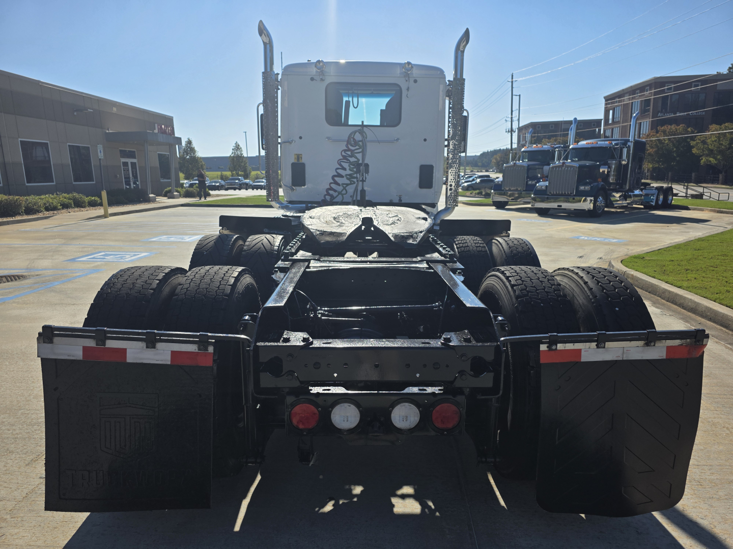 Kenworth T880 rear view showing fifth wheel, dual rear axles, and mud flaps with triplicate lights; cab back and exhaust stacks visible.
