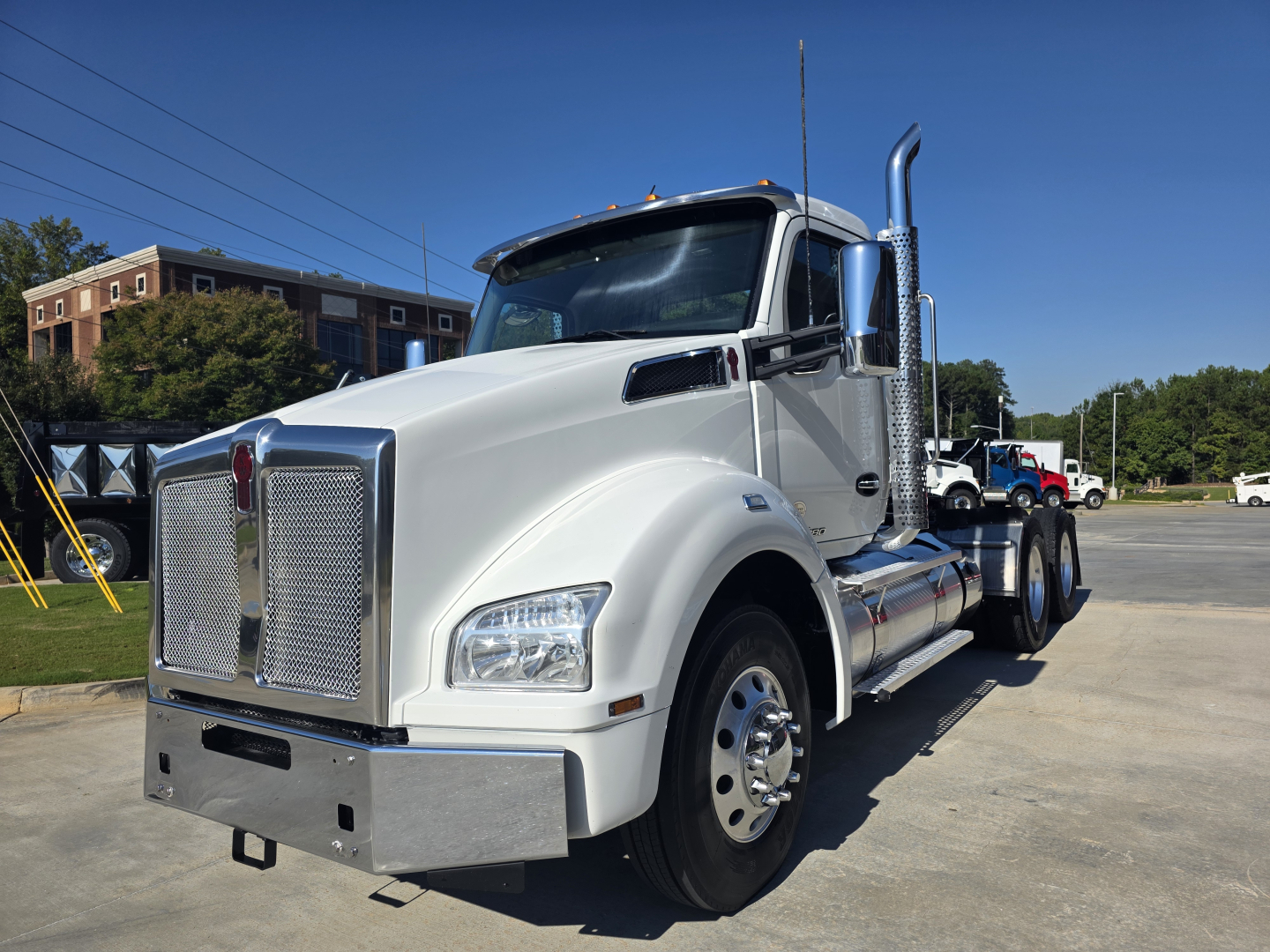 Kenworth T880 conventional daycab truck in a light silver color, front view showing large chrome grille, bumper, dual exhaust stacks, large side mirrors, and front fender with wheel.