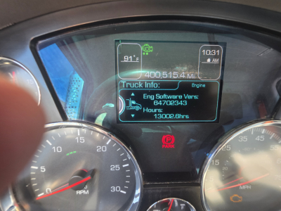 Kenworth T880 dash display showing truck information, engine software version, hours, and metric values with gauges in foreground.