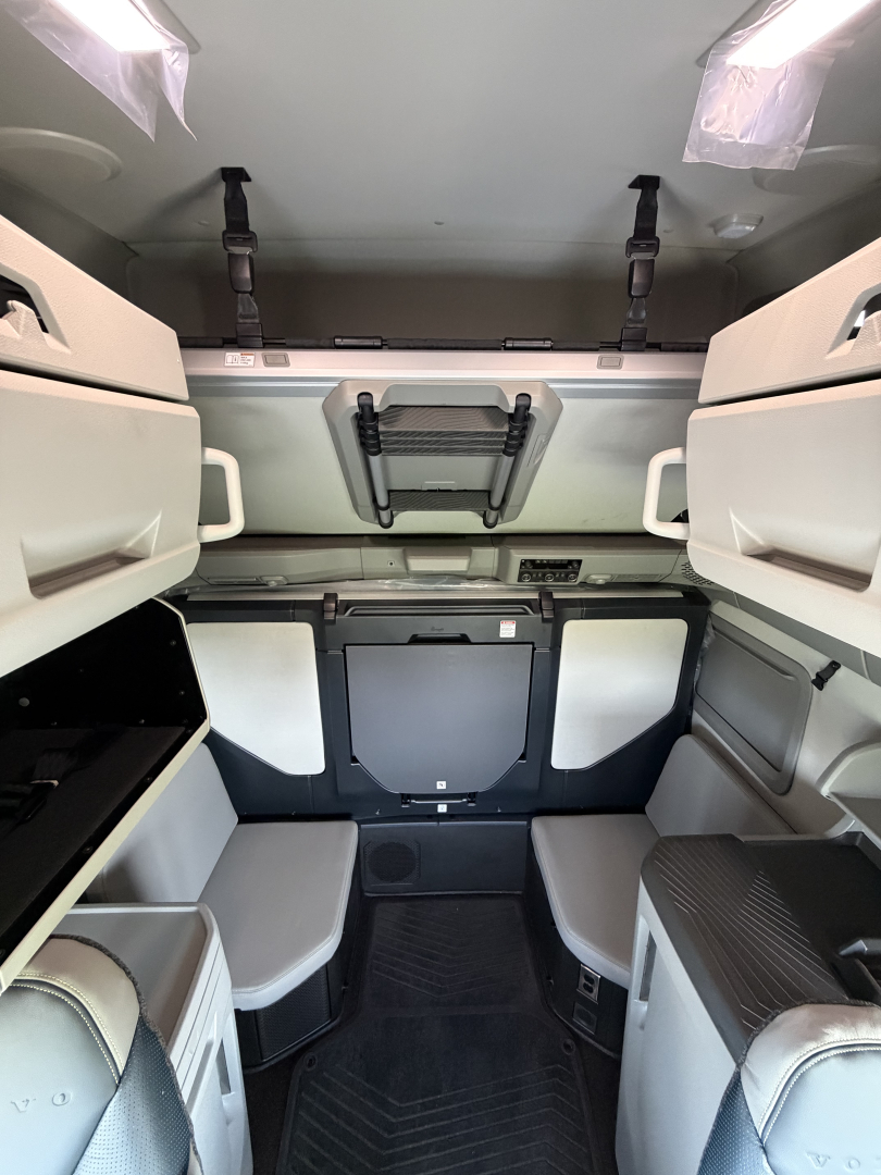 Volvo VNL64T860 cab interior showing sleeper area with storage cabinets, overhead bunk area, and steps. 