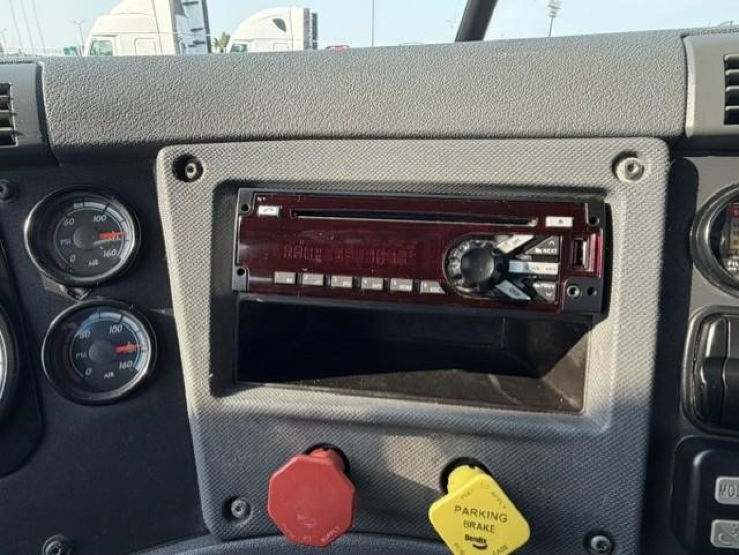 Dashboard panel of 2019 Freightliner Cascadia 126 showing aftermarket stereo head unit, red and yellow knobs, and gauges.