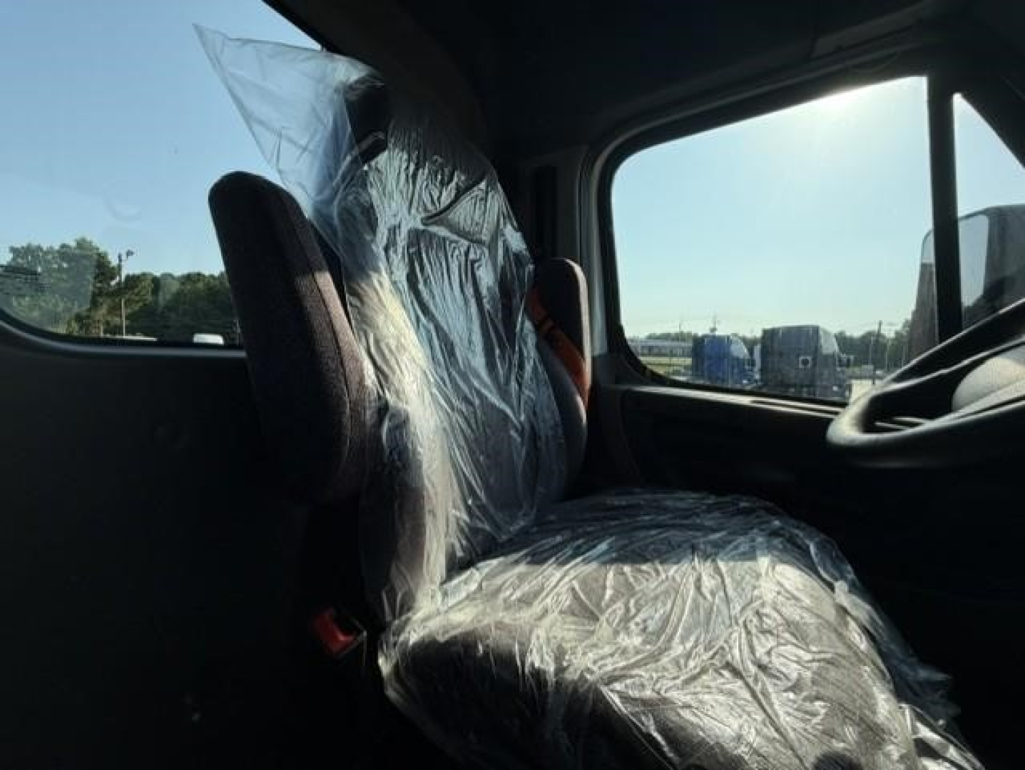 Freightliner Cascadia truck cab interior view showing plastic-covered seat and window with sunlight.