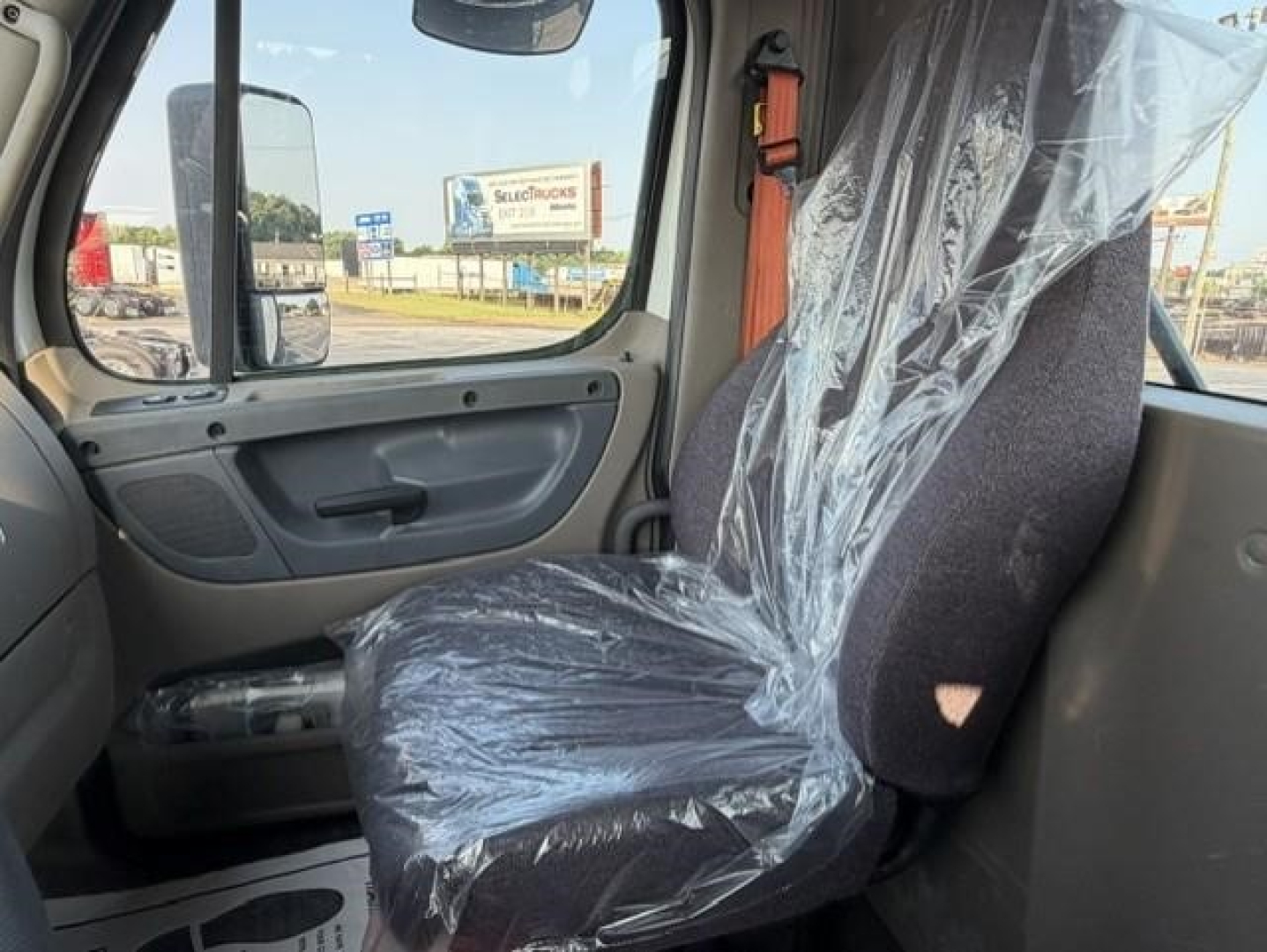 Freightliner Cascadia interior showing driver's seat wrapped in plastic and door panel.