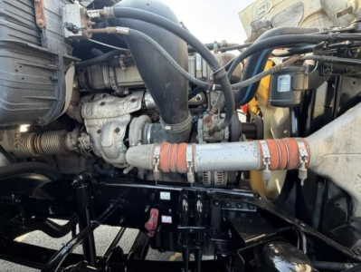 Freightliner Cascadia engine bay showing hoses, turbo, and intercooler piping with clamps; label stickers and black chassis components visible.