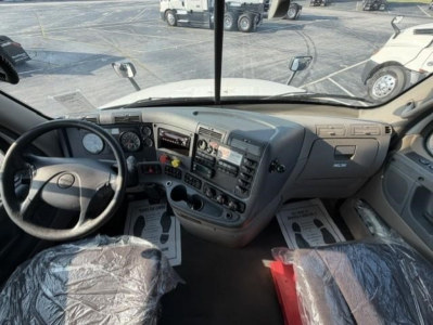 Cab interior of a Freightliner Cascadia 126 day cab showing steering wheel, dashboard, and driver and passenger seats covered in plastic.