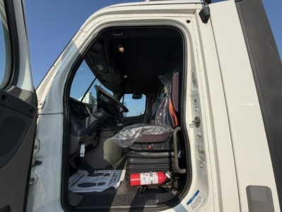 Truck cab interior with open door showing steering wheel, driver's seat wrapped in plastic, safety cone, and a fire extinguisher on the floor; windshield and dashboard visible.