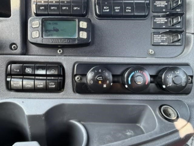 Dashboard controls of a Freightliner Cascadia truck showing digital display, air conditioning knobs, and various switches.