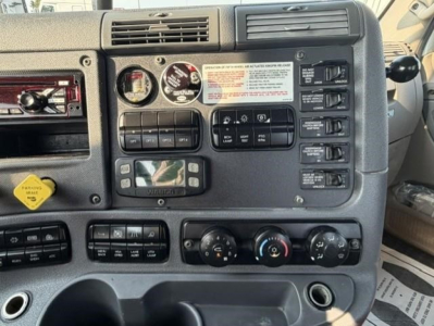 Dashboard and controls of a Freightliner Cascadia day cab showing warning labels, switches, and dials.