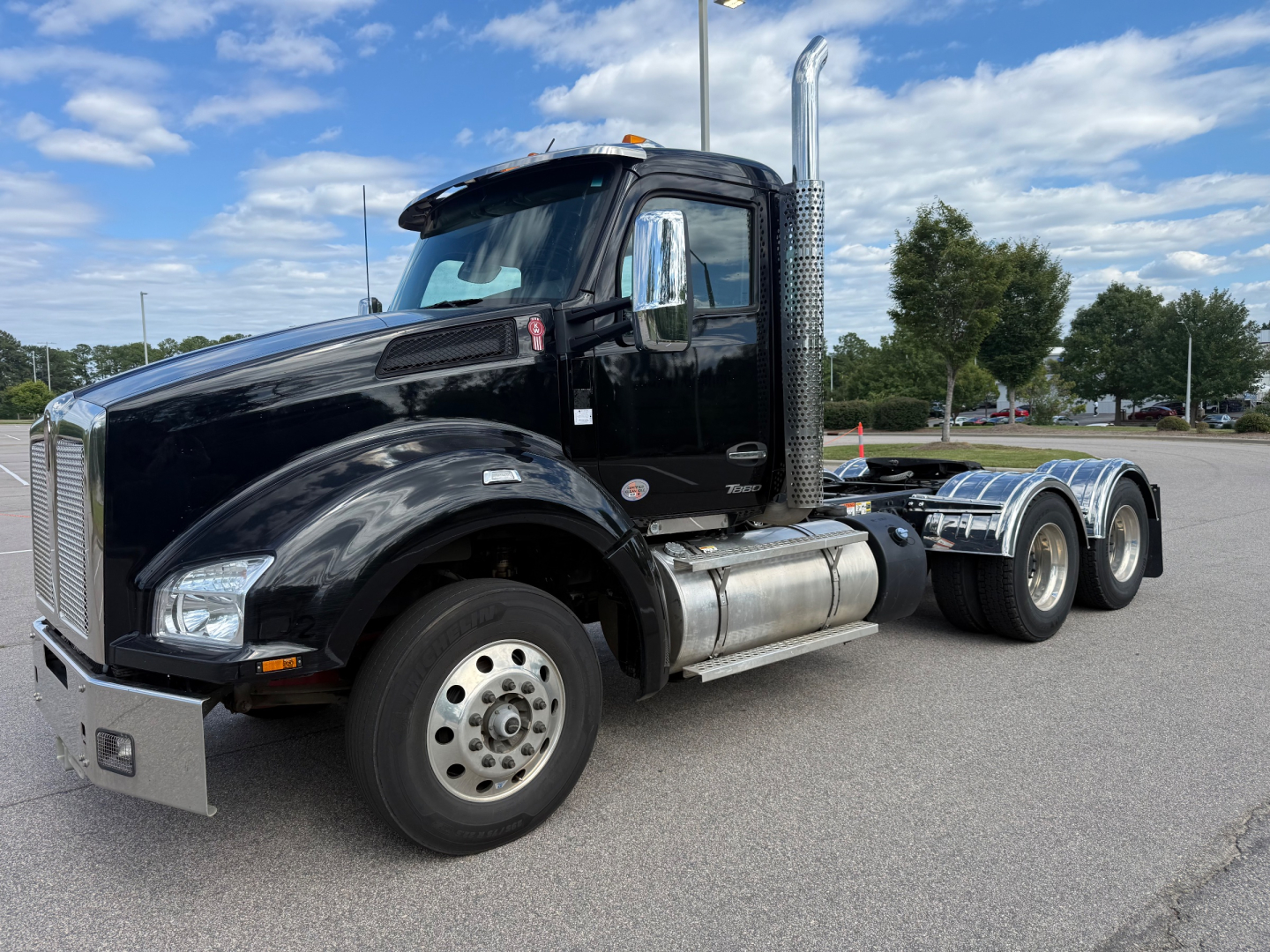 Kenworth T880 conventional daycab truck, black cab, chrome exhaust stack, dual rear axles, front-left view.