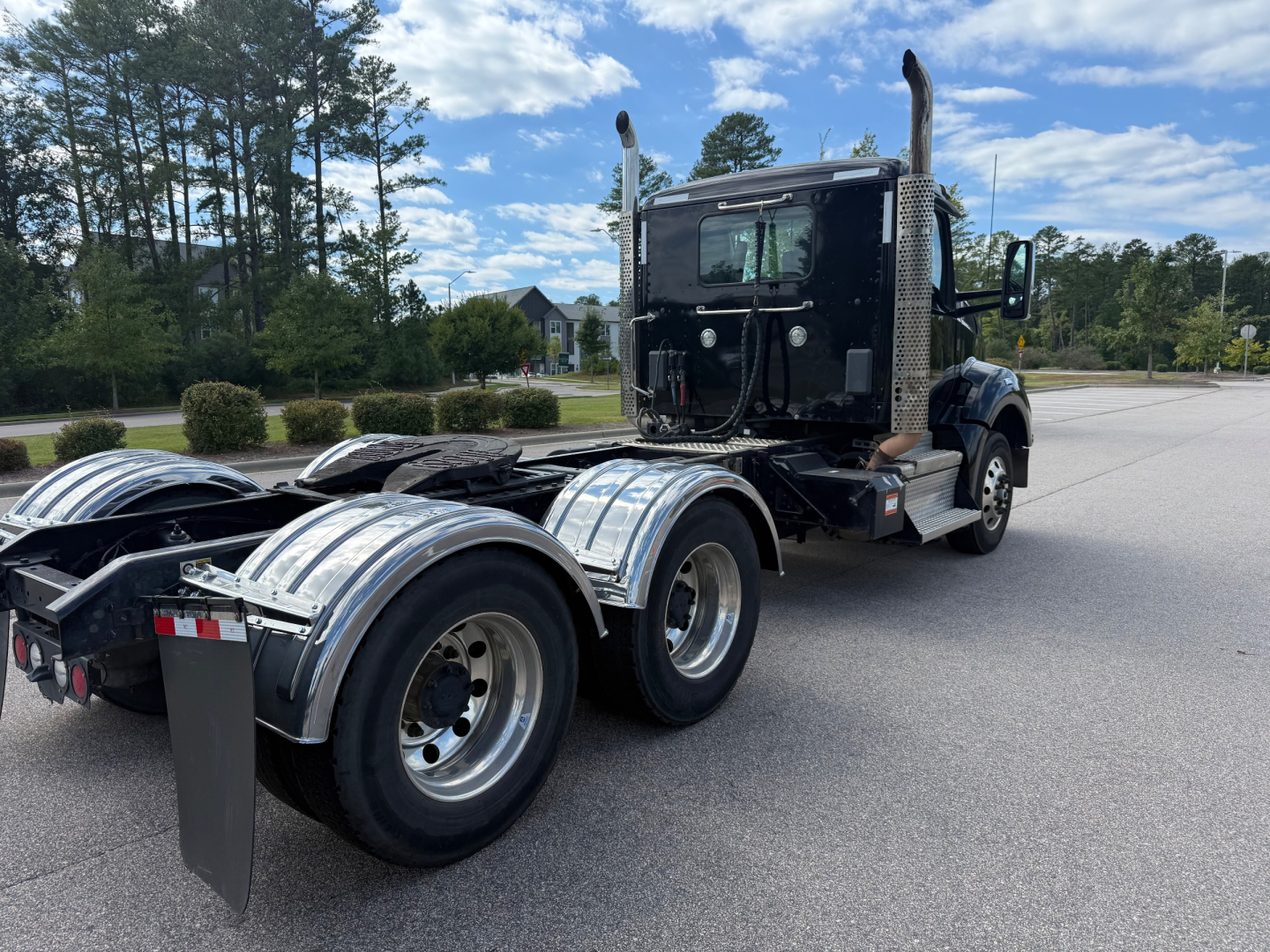 Kenworth T880 daycab tractor side/rear view showing dual rear axles, chrome fenders, diesel fuel tanks, and rear engine area with sleeper cab in black.