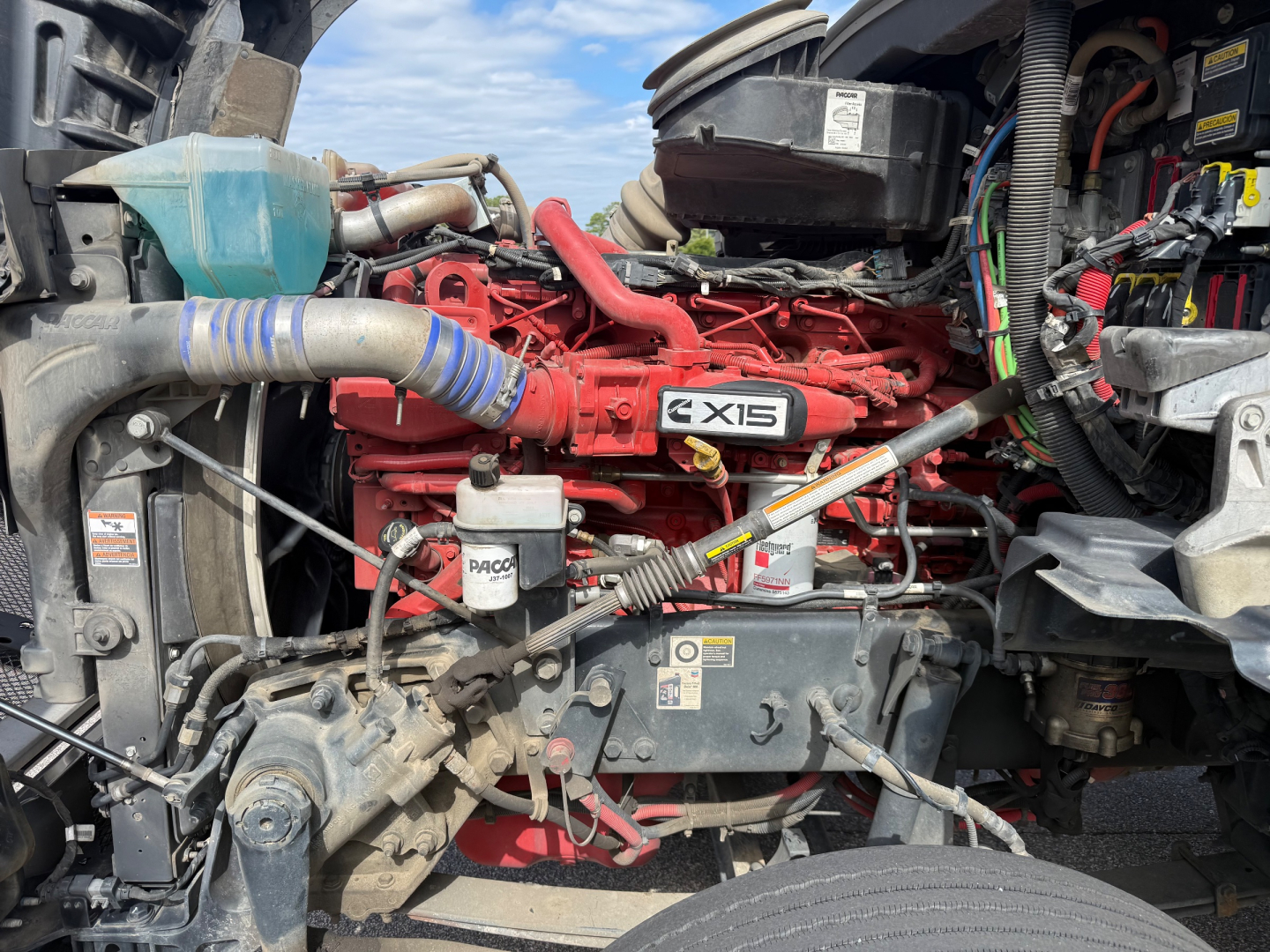 Kenworth T880 engine bay with red Cummins ISX15 engine, various hoses, battery, and wiring harness visible.