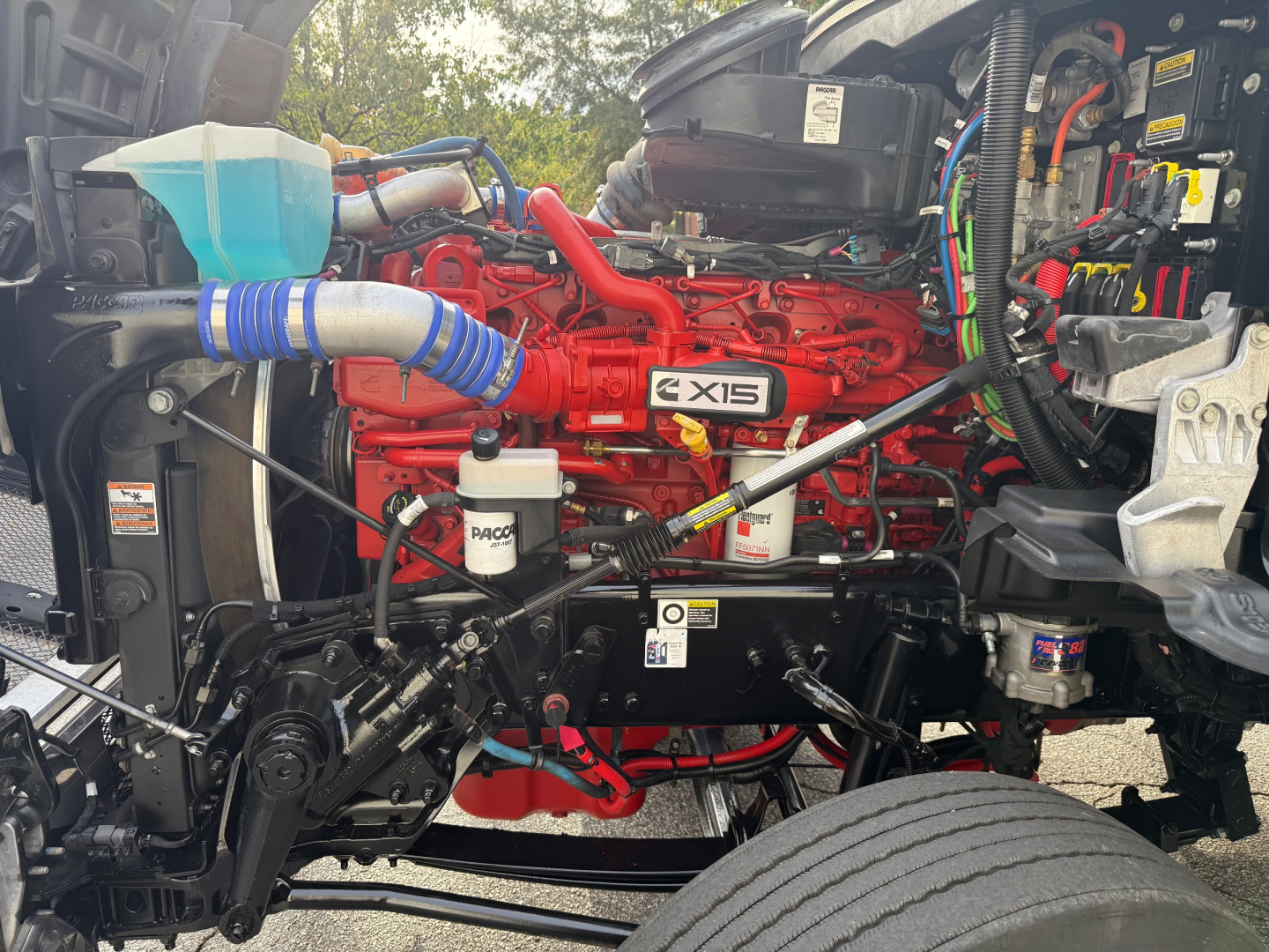 Kenworth T880 engine bay showing red X15 engine, blue coolant reservoir, turbo hoses, and various hoses and components.