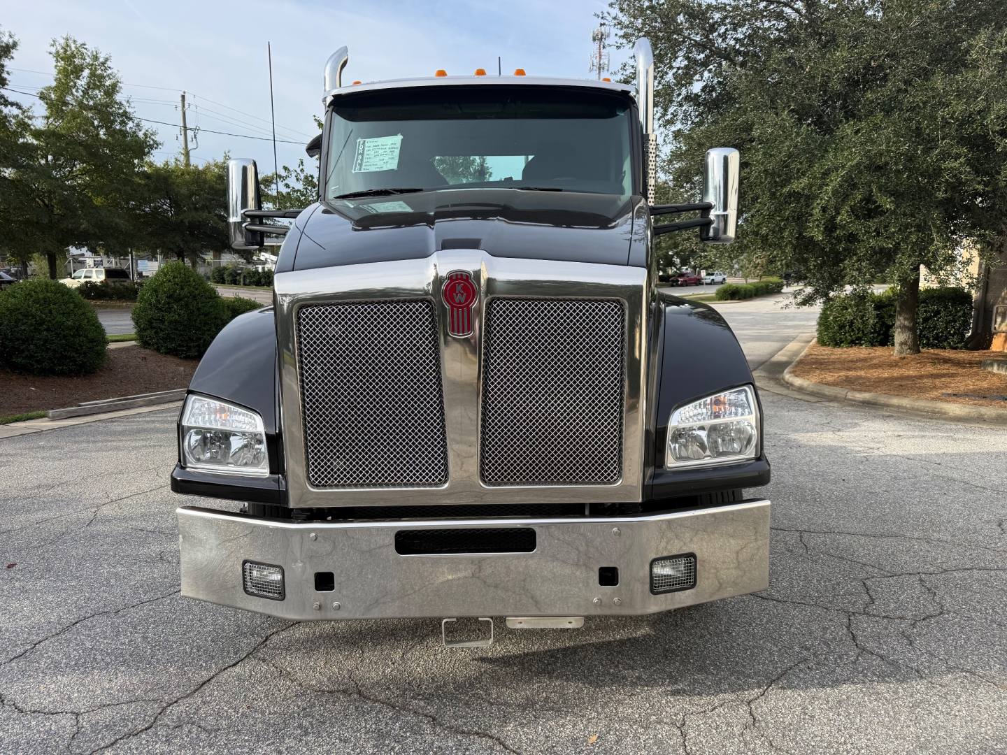 Kenworth T880 cab front view showing large chrome grille, badge centered, rectangular headlights, silver bumper, and side mirrors.