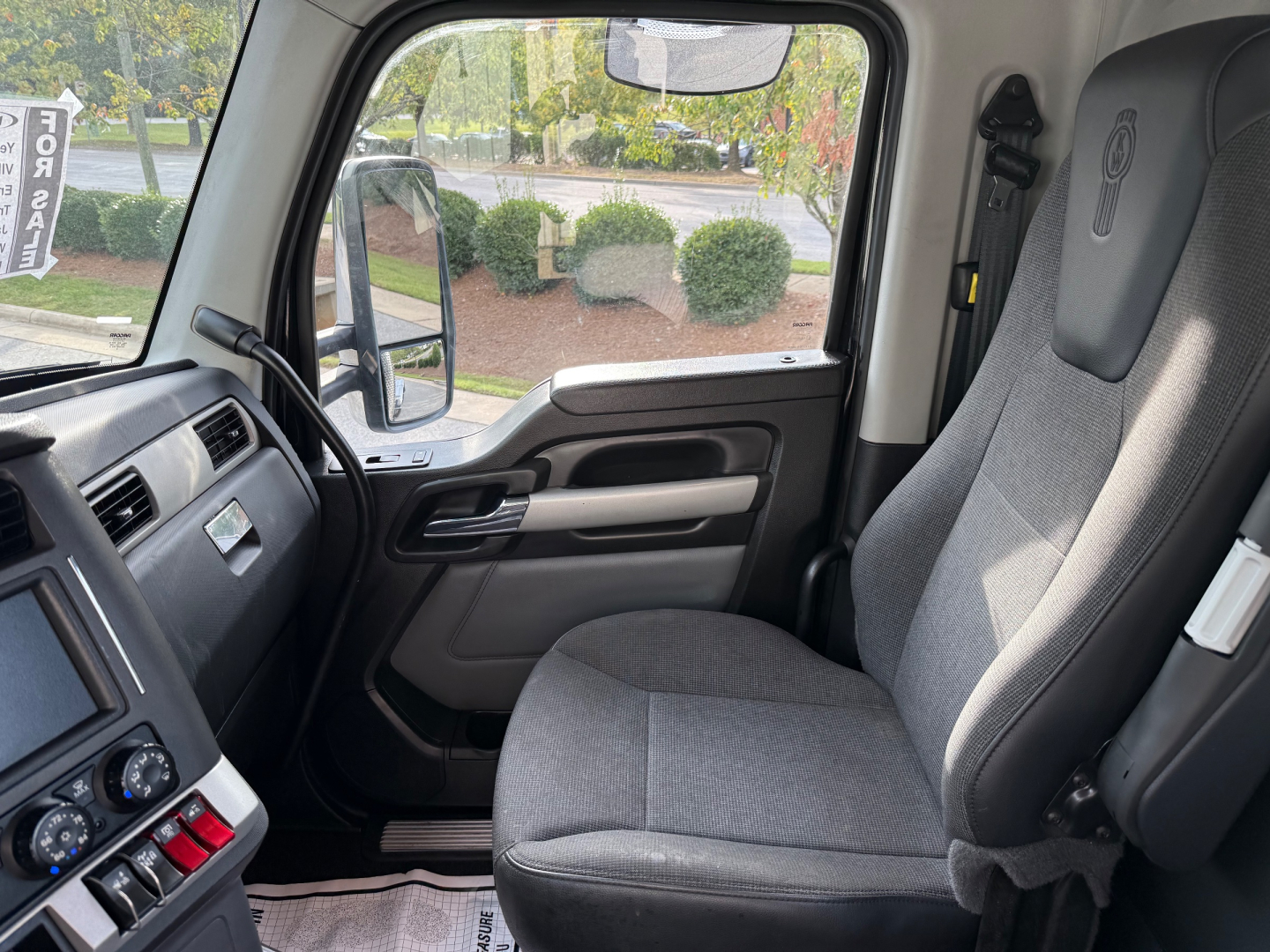 Kenworth T880 truck interior cabin view showing driver seat and dashboard with steering wheel and side window.