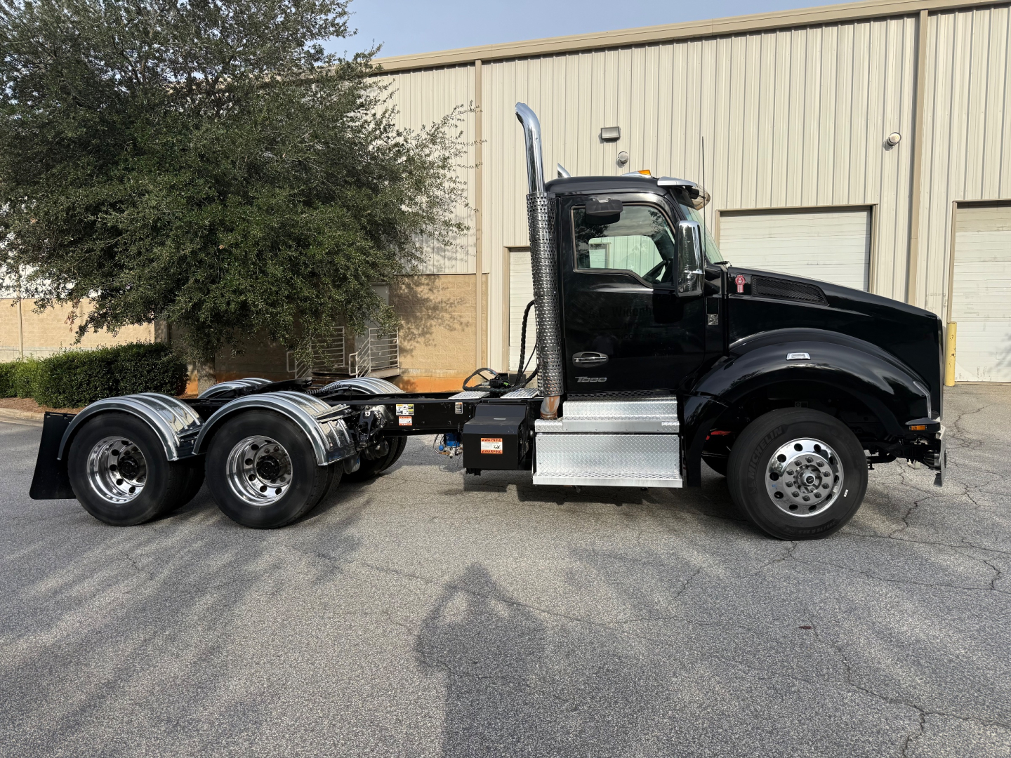 Kenworth T880 6x4 tractor side profile with black cab, chrome exhaust stack, dual rear axles, and metal step; no visible text on side besides truck features.