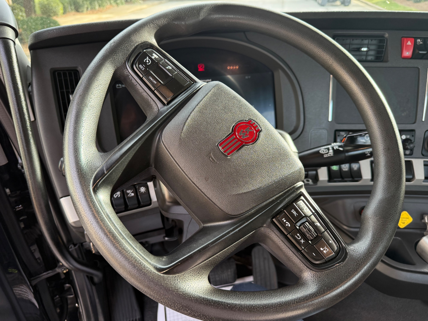 Steering wheel and dashboard in a Kenworth T880 cab showing control buttons and instrument cluster with logo on steering wheel.