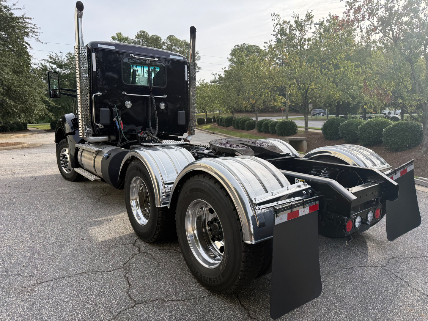 Kenworth T880 cab with dual rear axles showing chrome fuel tanks, mud flaps, and rear hitch area; side and back view of tractor chassis.