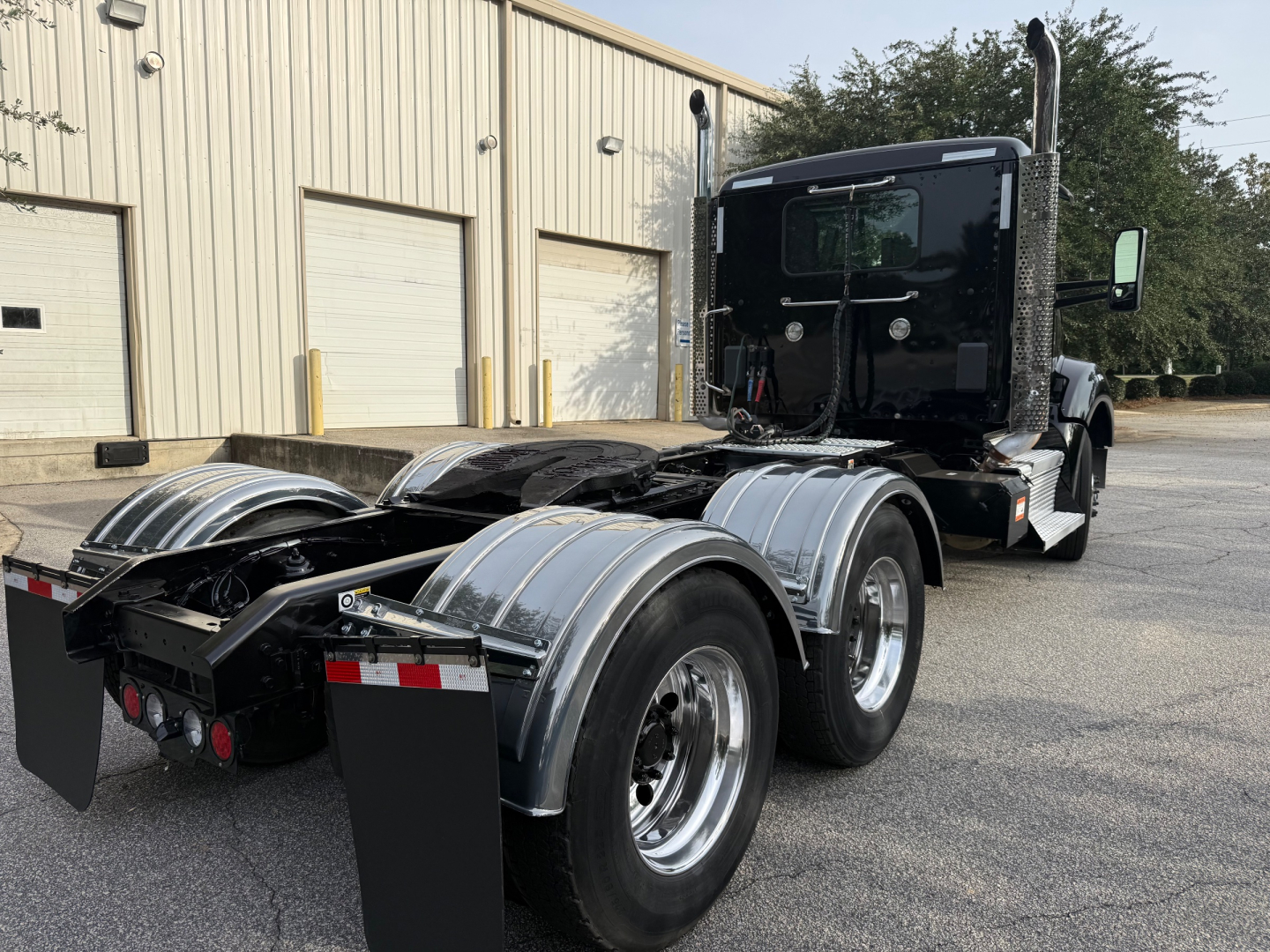 Kenworth T880 semi truck rear view showing dual rear axles with polished aluminum fenders and fifth wheel hitch, black cab, factory exhaust stacks.