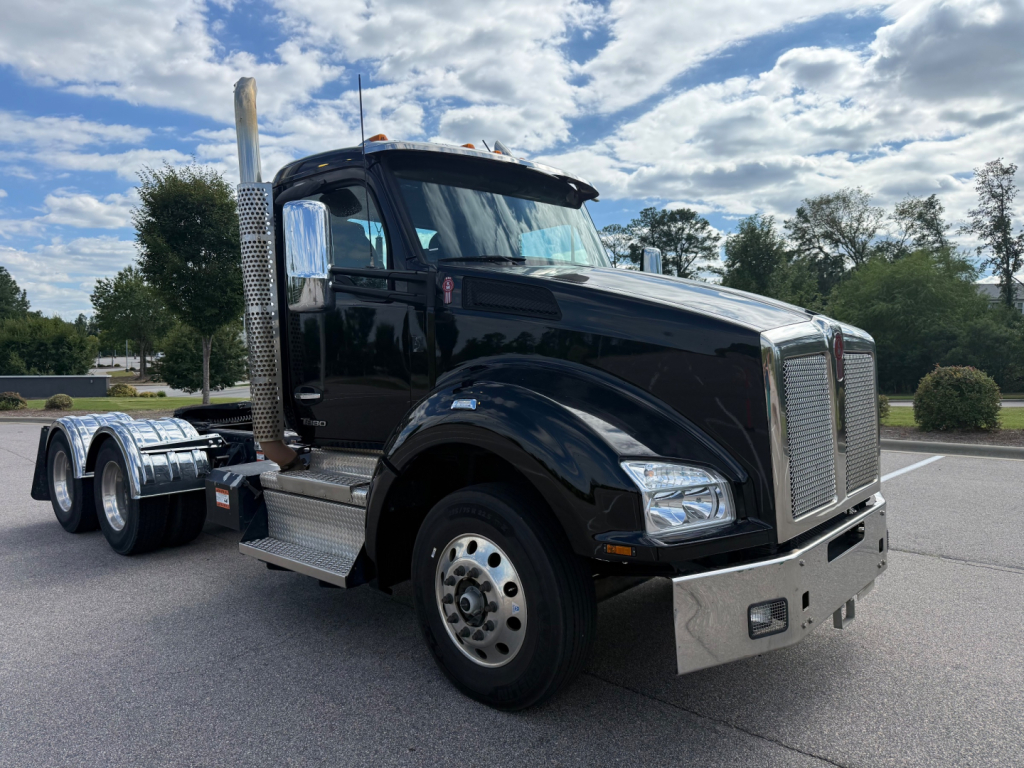 Kenworth T880 conventional daycab truck in black, front three-quarter view, chrome grille, vertical exhaust, large fuel tanks, dual rear axles.