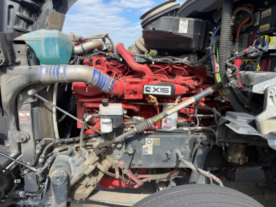 Kenworth T880 engine bay with red Cummins ISX15 engine, various hoses, battery, and wiring harness visible.