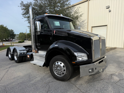 Kenworth T880 conventional daycab truck in black, front-left view, showing chrome grille, large exhaust stack, dual rear axles, chrome bumper, and side steps.
