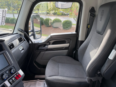 Kenworth T880 truck interior cabin view showing driver seat and dashboard with steering wheel and side window.