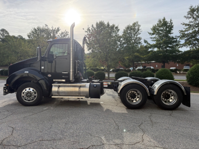Side view of a black 2024 Kenworth T880 conventional daycab tractor, dual rear axles, chrome fuel tanks, exhaust stacks, and aluminum wheels.