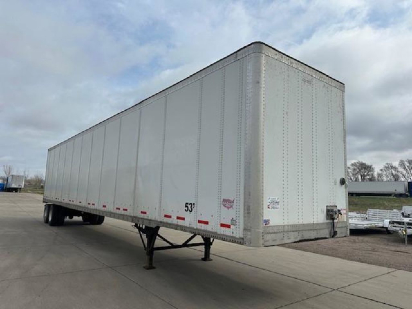 Trailer view showing a 53-foot Wabash box trailer with support legs down. Visible markings include '53'' near front bottom edge, side riveted aluminum panels, rear doors, and small decals near the front corner.