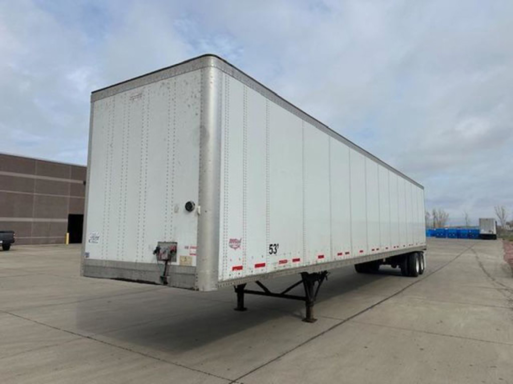 Trailer body showing a 53' dry van with wheels underneath and landing gear in a parking lot.