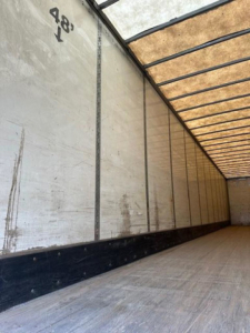 Trailer interior wall and ceiling of a 2014 Wabash van trailer showing plywood floor and side walls with black rubber strip at base.
