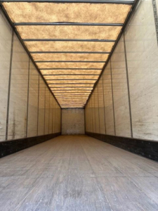 Interior of a trailer viewed from the back, showing a long wooden roof and metal sidewalls with a worn wooden floor.