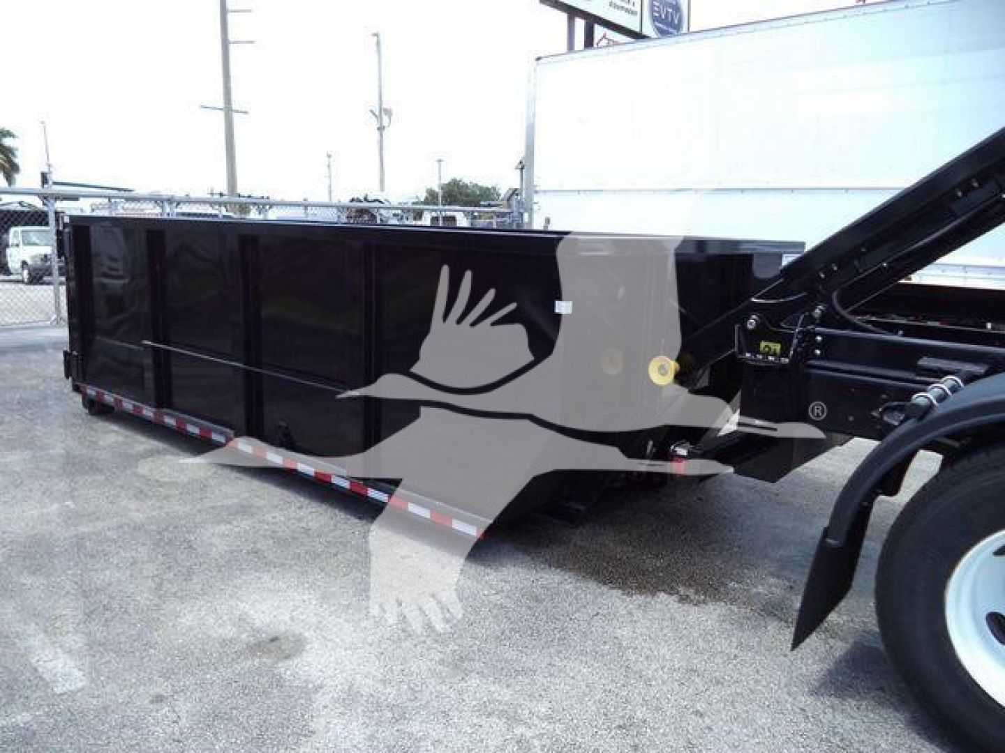 Dump trailer with side panel, showing black painted dumpster/dump bed and hitch area; no legible labels or serials visible on the side.