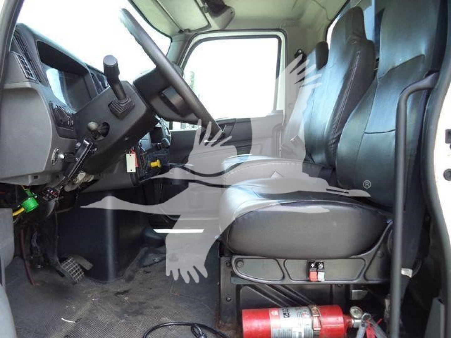 Truck cab interior of a 2019 International 4300 roll-off showing steering wheel, dashboard, and driver seat with a red fire extinguisher mounted under seat.