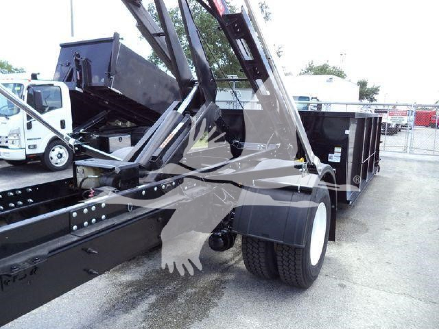International 4300 roll-off truck with hydraulic lift arm and dumping container, side view showing rear dual tires and chassis components.