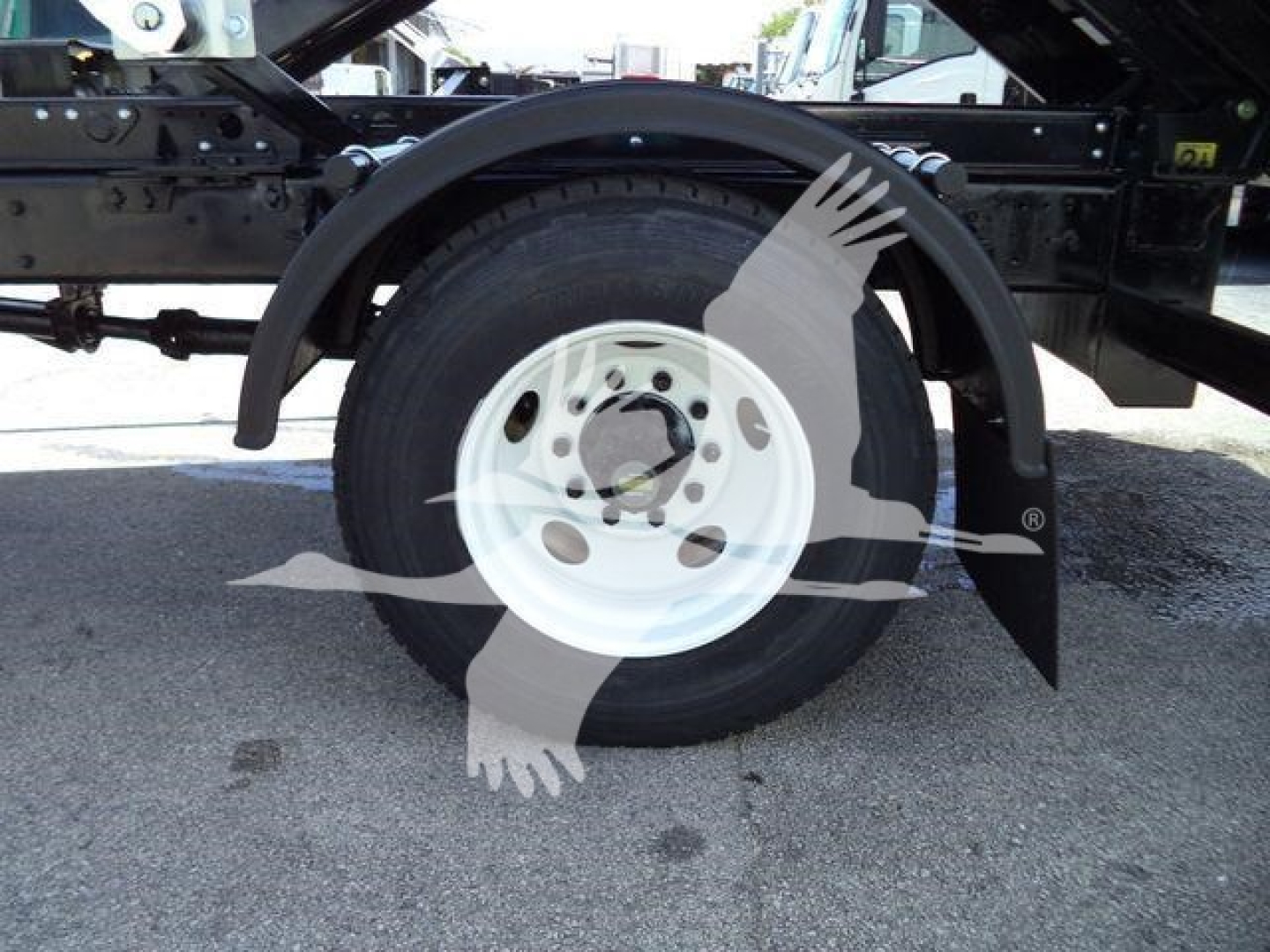 Truck wheel and suspension undercarriage with white steel wheel and black frame, branding watermark visible overlay.