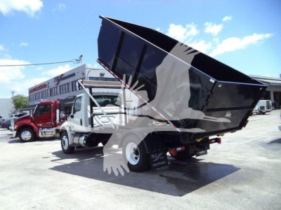 Dump truck with hydraulic lift in raised position, rear dump bed tilted open, International 4300 roll-off chassis visible