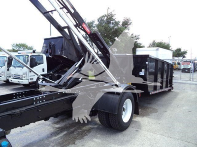 International truck in yard showing roll-off truck body and crane structure with black trailer. Visible labels: no legible brand text besides truck setup.