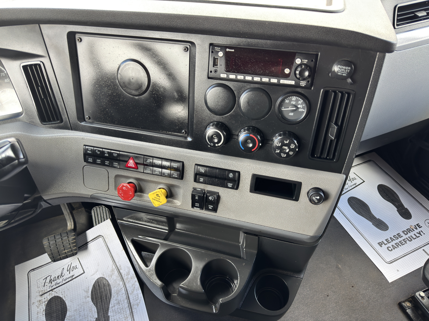 Cab interior of a 2022 Freightliner Cascadia 126 showing dash panel with radio, gauges, climate controls, hazard switch, cup holders, and pedal area.