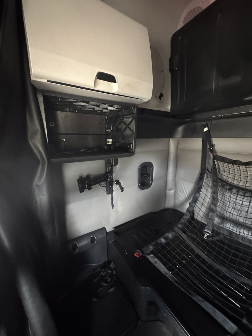 Cab interior of a 2022 Freightliner Cascadia 126 sleeper showing dash console area, open glovebox, and bunk area with safety netting and metal framework.