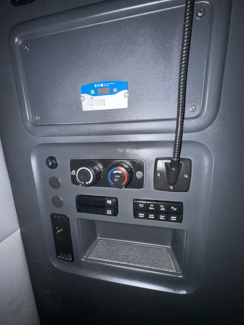 Dashboard panel inside a Freightliner Cascadia showing climate controls and switches with a blue sticker above; circular climate control dials and multiple rectangular buttons.