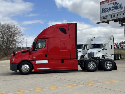 Freightliner Cascadia 126 truck in red sleeper cab with white trailers in background, side view.