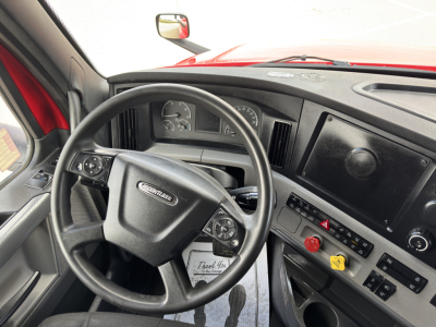 Cab interior of a Freightliner Cascadia showing steering wheel with Freightliner logo, dashboard gauges, and center console with controls and warning lights.