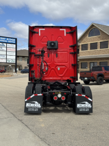 Rear view of a red Freightliner Cascadia truck cab with chassis and dual rear axles, mud flaps, and dealership branding visible.