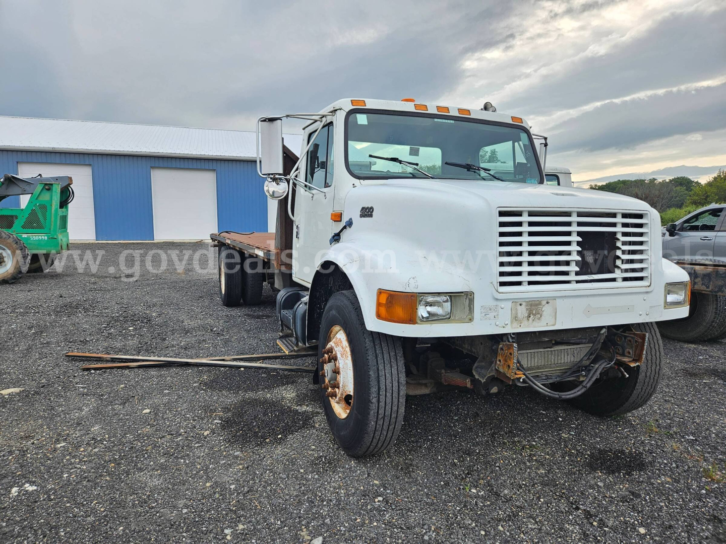 International 4900 flatbed dump truck in view showing front grille, headlights, and bumper with some rust; side mirrors; hoisted bed area visible; tires and wheel hubs; VIN plate and stock number not legible.