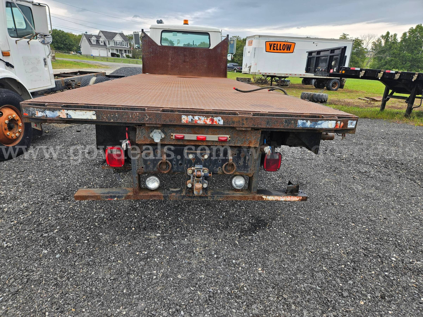 Flatbed dump truck bed rear view of a 1995 International 4900 showing rusted metal flatbed, tail lights, hitch, and hydraulic components.