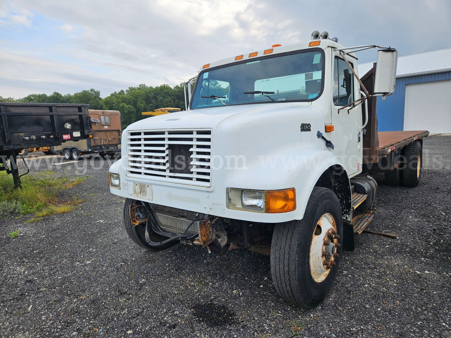 International 4900 flatbed dump truck in a yard, front grill, dual rear wheels, white cab, flatbed in back, stock photo watermark