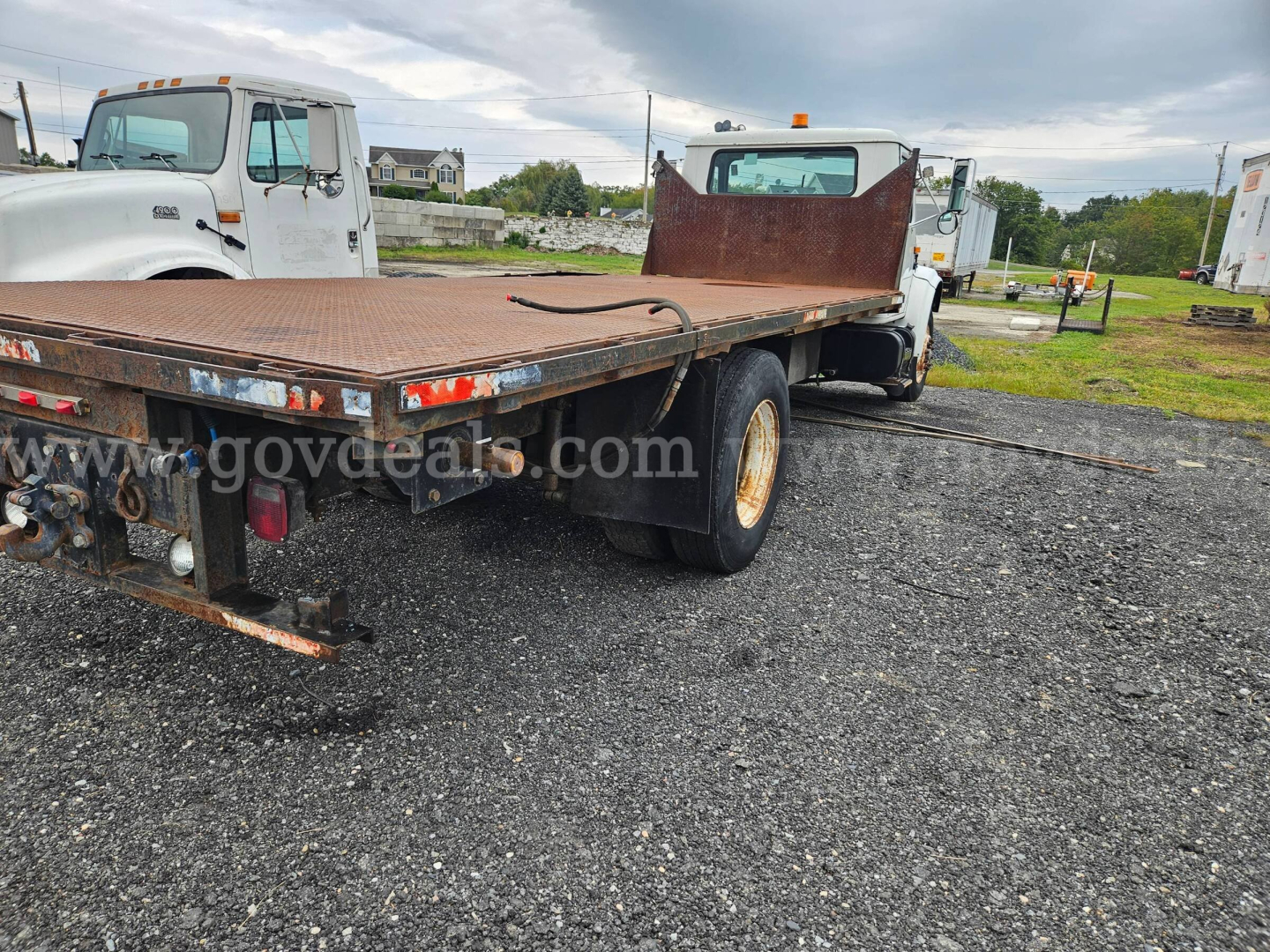Flatbed dump truck rear and cargo deck showing steel flatbed with hydraulic hydraulics, dual rear wheels, and rear lights in a vehicle lot.