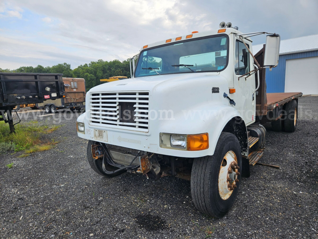 International 4900 flatbed dump truck in a yard, front grill, dual rear wheels, white cab, flatbed in back, stock photo watermark