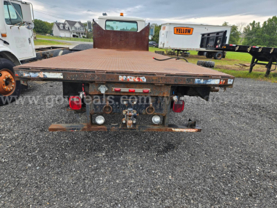Flatbed dump truck bed rear view of a 1995 International 4900 showing rusted metal flatbed, tail lights, hitch, and hydraulic components.