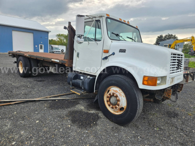 International 4900 flatbed dump truck in-service showing front grille, cab, and long flatbed with wheel wells and rust on rims.
